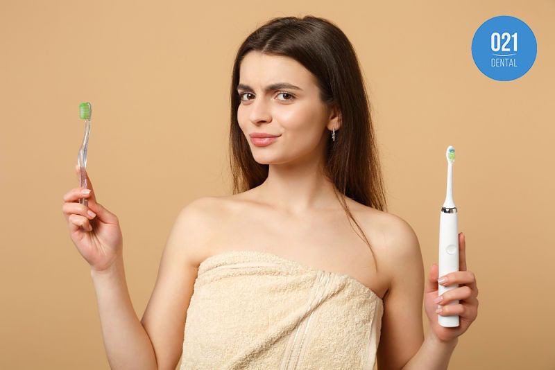 Mulher segurando escova de dentes elétrica e tradicional em cada uma das mãos
